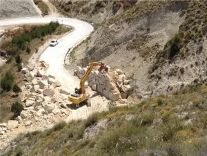 Retroexcavadora colocando bloques de escollera junto a una carretera de montaña