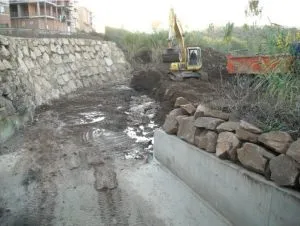 Retroexcavadora colocando escollera en la margen de un cauce