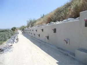 Muro de hormigón con anclajes junto a un camino